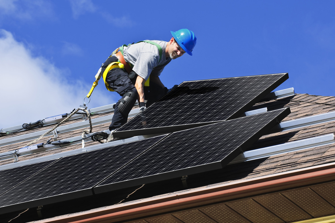 A man on the roof of a house with a power tool.